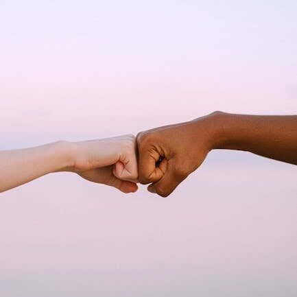 pexels-photo-4672718-4672718 Two diverse hands fist bump against a soft pastel background, symbolizing unity and friendship.